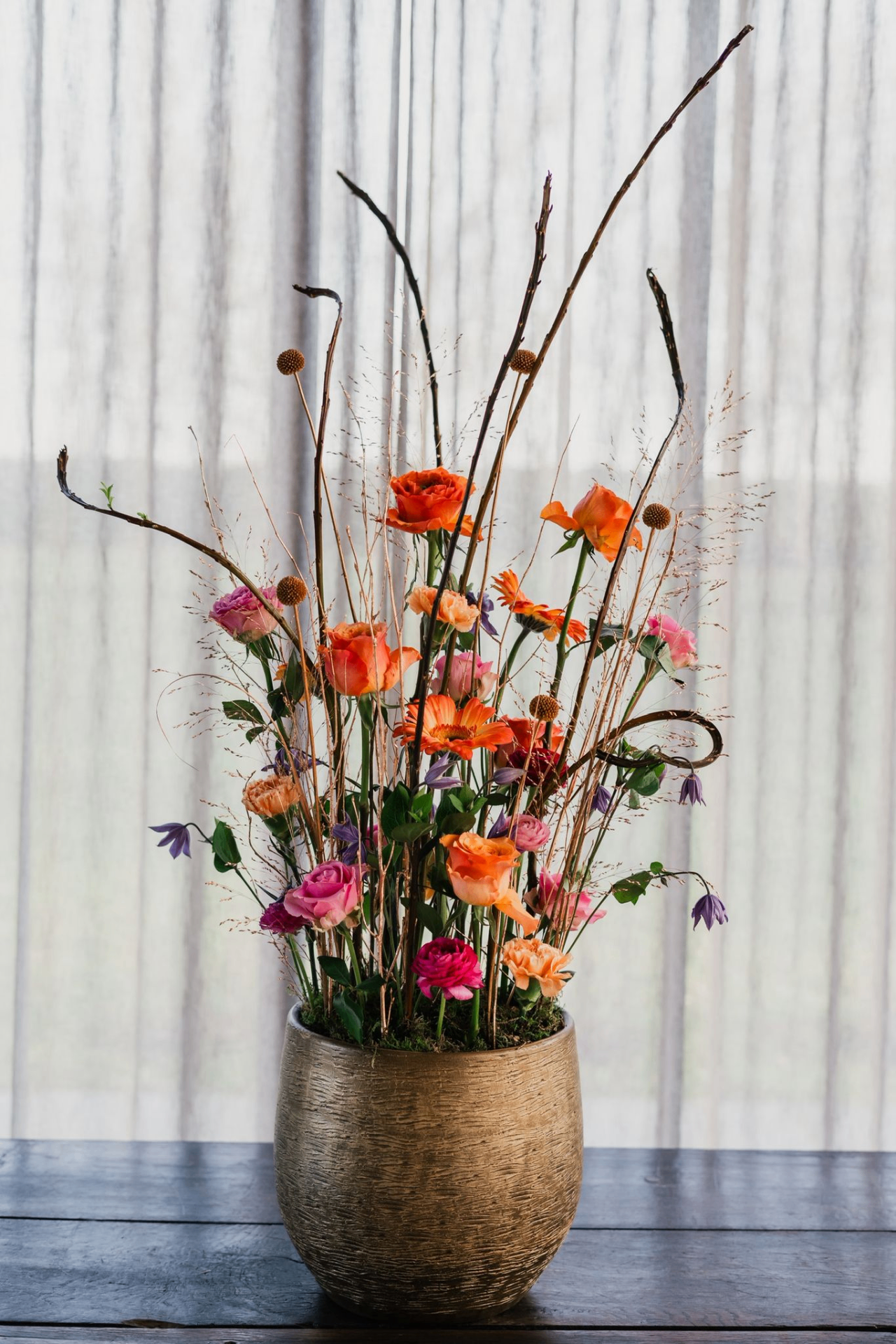 Kleurrijk bloemstuk in een gouden vaas met takken en seizoensbloemen